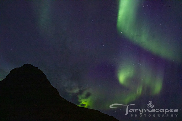 Whirls of green and purple dance in front of a mountain's silhouette