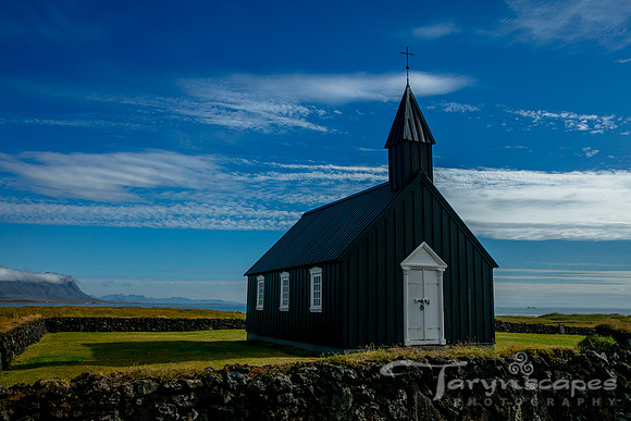 A black church with a white door stands alone against a deep blue sky with wispy clouds.