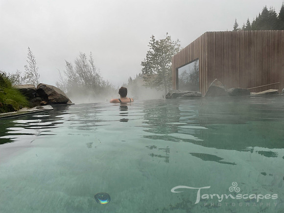 My darkhair is twisted up and I stand, underwater at the edge of an infiniti ledge into the trees. Steam rises off the teal lagoon water.