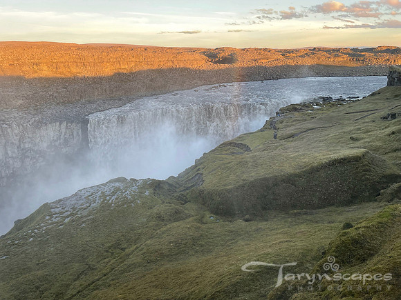 A powerfall waterfall surrounded by greenish rocks and harsh orange light from the sun.