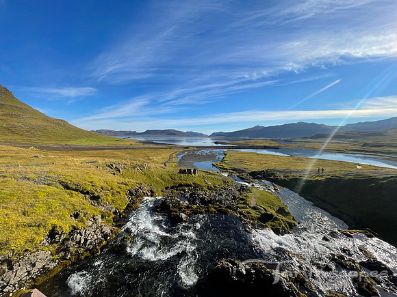 The edge of a green mountain touches the river running along side it. Wispy clouds float in a deep blue sky