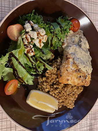 A plate of chicken with a cream sauce sits at top farro. A green leaf salad with blue cheese and balsamic.