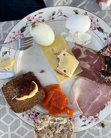 Breakfast plate of hardboiled egg, dark geysir bread with butter and jam, cold cuts and cheeses