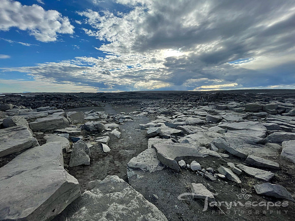 Flat rocks span the landscape while puffy clouds spot the blue sky