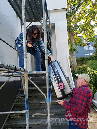 I'm standing on a scaffold, bent over grabbing my large suitcase from my dad who is standing on the ground hoisting it up.