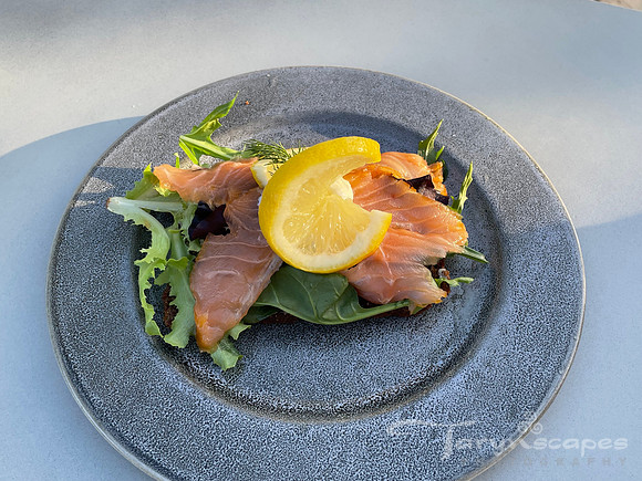 Greens topped with pink cold smoked salmon topped with a lemon wedge