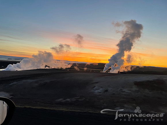 Steam as thick as smoke rises from the earth, backlit by a golden, pink and blue sunset.