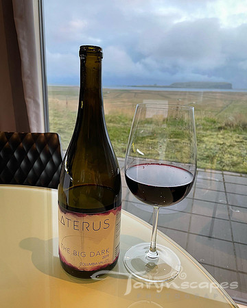 Laterus The Big Dark wine bottle next to a glass of wine with the black sand beach hills in the back