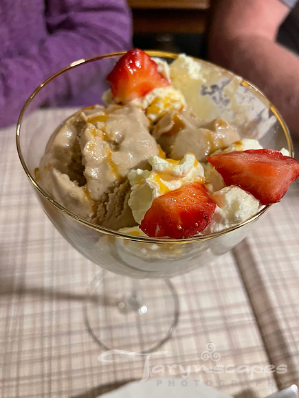Chocolate icecream in a  glass with a stem with strawberries, caramel and whipped cream