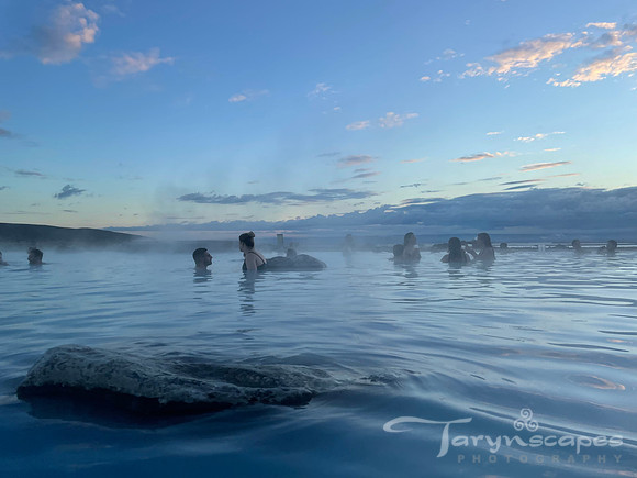 A dozen people submerged in the hot springs silhouetted against a fading blue sky.