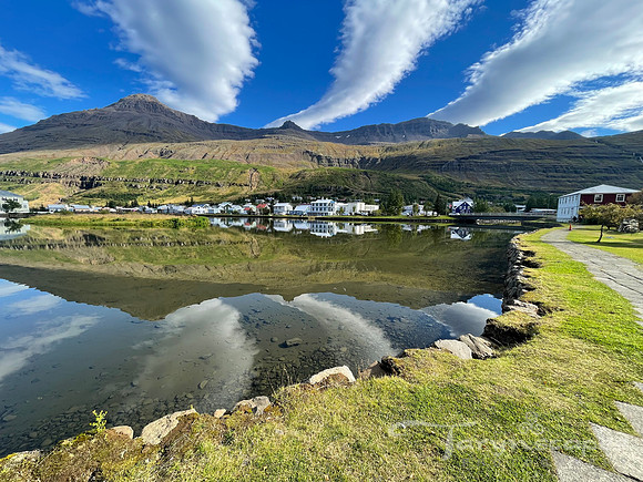 Still lake showing the reflection of the mountain and houses and streaks of clouds