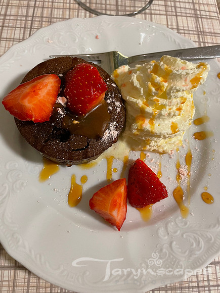 Dark chocolate cake smothered in caramel and strawberries with whipped cream on the side