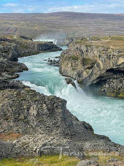 Milky teal water flowing from Godfoss down between the two rocky cliffs of the river