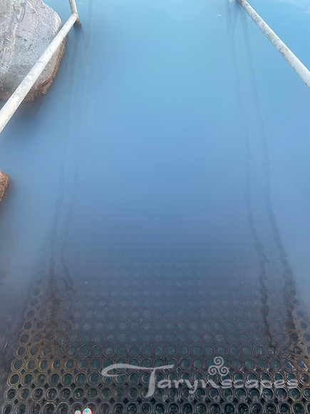Metal stairs go down into a milky teal water