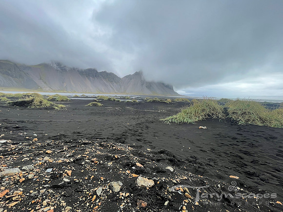 black sand beach with spots of mossy hills. Above stormy sky and mountains towering in the distance