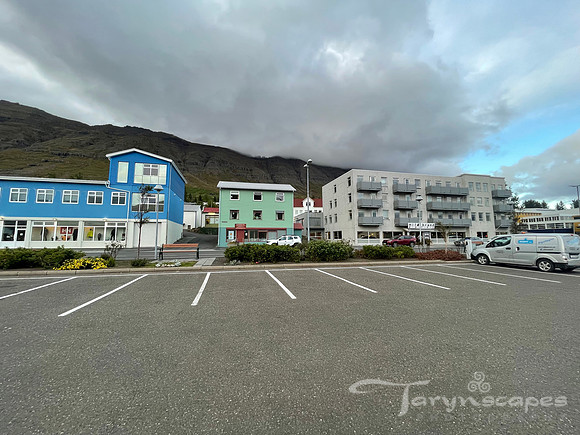 Parking lot with a blue, seafoam green and white buildings.