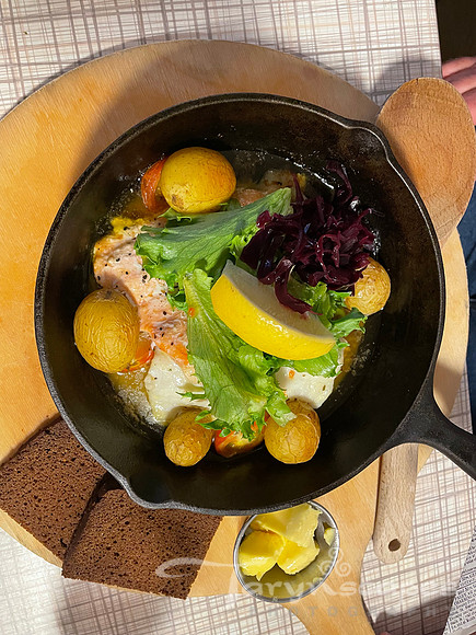 Small skillet with potatoes, fish, greens and lemons with a side of dark bread and butter