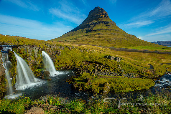 Waterfalls in the foreground while a mountain looms in the background against a blue sky